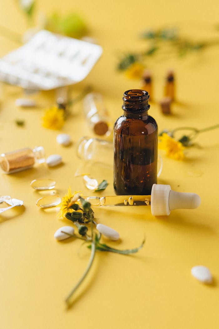 Services Brown glass dropper bottle among herbs and pills on yellow surface, ideal for wellness themes.