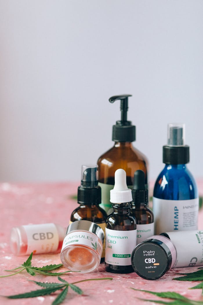 Services A variety of CBD products including oils and capsules on a textured pink surface with leaves.